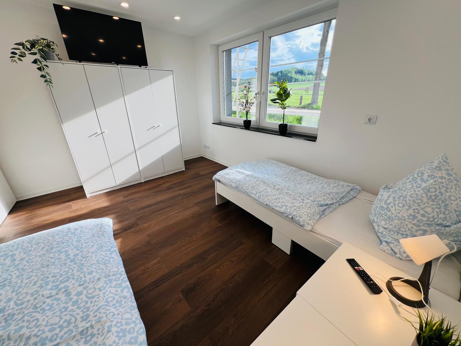 Modernes, helles Schlafzimmer mit guter Ausstattung, zwei Betten, großem Kleiderschrank und praktischem Schreibtisch — sehr wohnlich wirkendes Monteurzimmer.