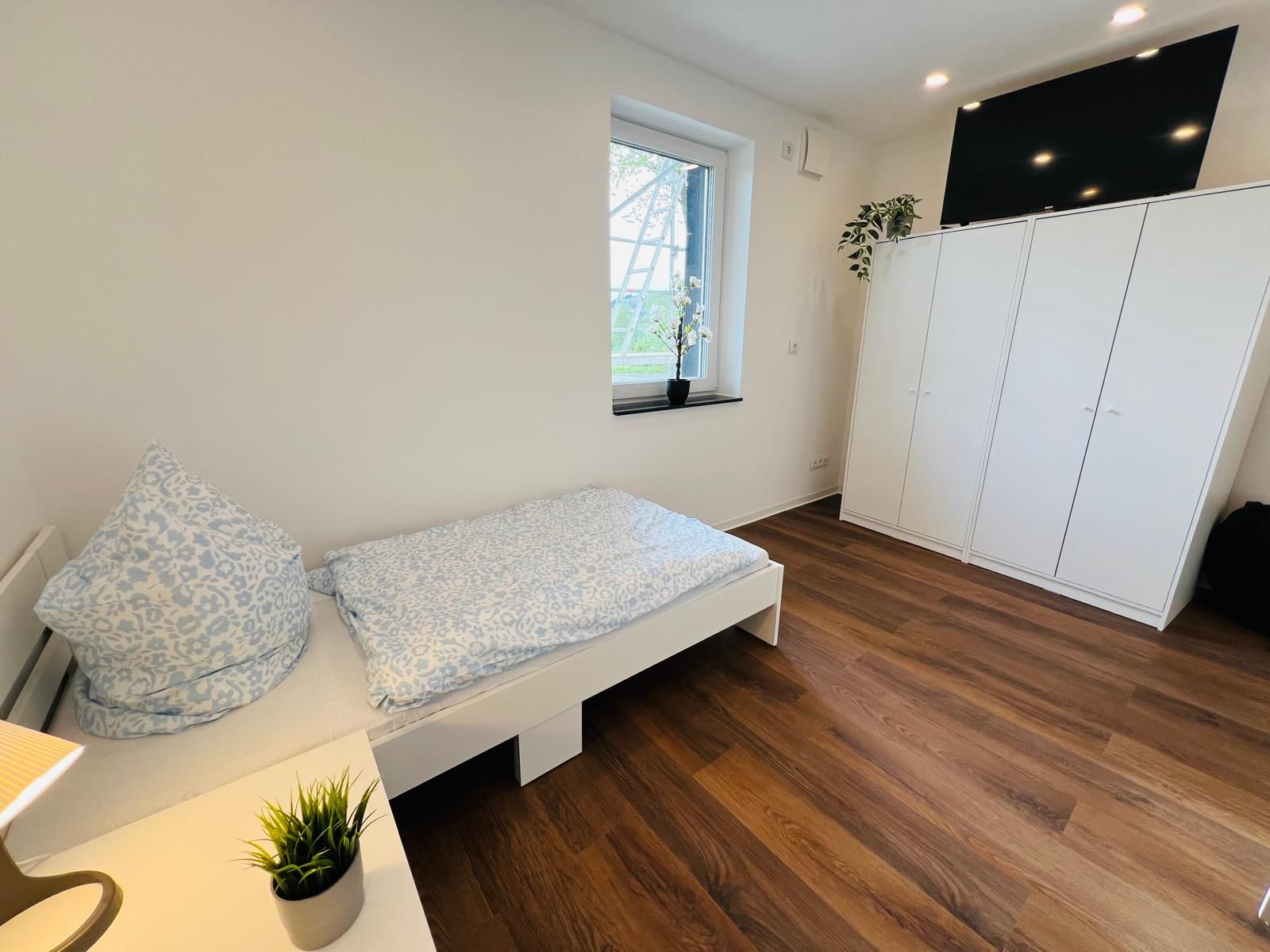 Modernes, helles Schlafzimmer mit komfortabler Ausstattung — gemachtes Bett, großer Kleiderschrank und TV sorgen für gute Funktionalität.